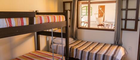 A dormitory room with bunk beds, a window with curtains, and a view of an outdoor area with tables and chairs.