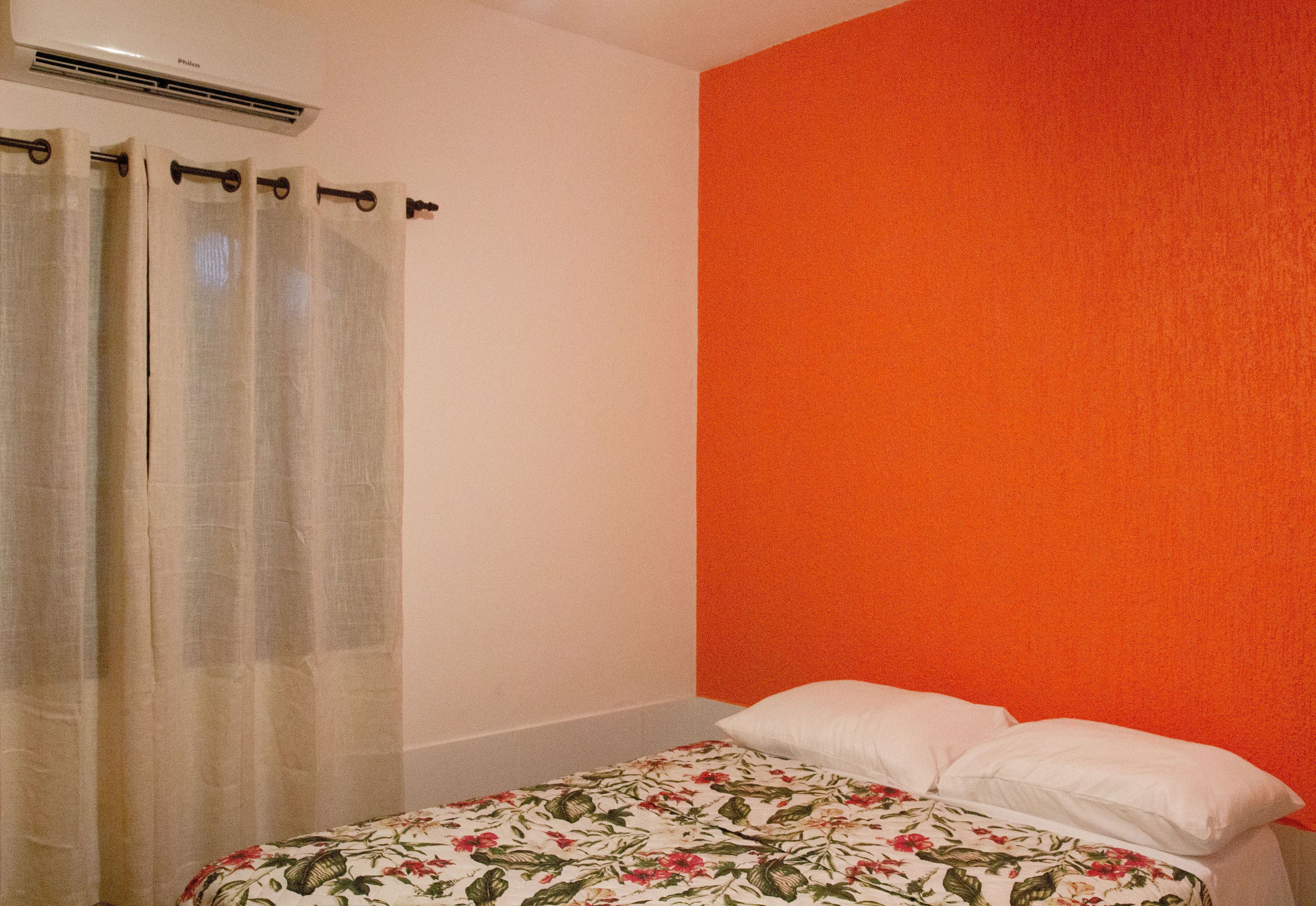 Un dormitorio con cama, almohadas blancas, colcha estampada, cortina de ducha y equipo de aire acondicionado.