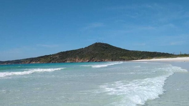 A beach with clear turquoise water, a sandy shore, and a hill in the background. - Beach Hostel & Suites, Cabo Frio (Cabo Frio)