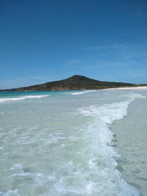 A beach with clear turquoise water, a sandy shore, and a hill in the background. - Beach Hostel & Suites, Cabo Frio (Cabo Frio)