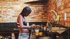A person preparing food at a kitchen counter with a brick wall background and a sign that reads "MANTENHA LIMPO". - Beach Hostel & Suites, Cabo Frio (Cabo Frio)