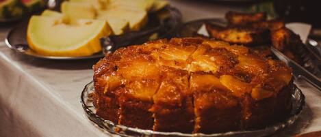 A dessert dish with a caramelized top, accompanied by sliced apples and a glass of beverage on a table.