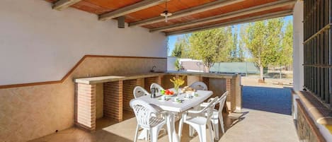 Eine Terrasse im Freien mit Grillplatz aus Ziegelsteinen, weißen Plastikstühlen und einem Esstisch.