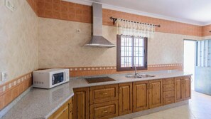 A kitchen with wooden cabinets, a microwave, a stainless steel sink, and a window with a curtain.