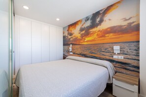 Un dormitorio con cama, mesita de noche, enchufe en la pared y una puerta con panel de vidrio.