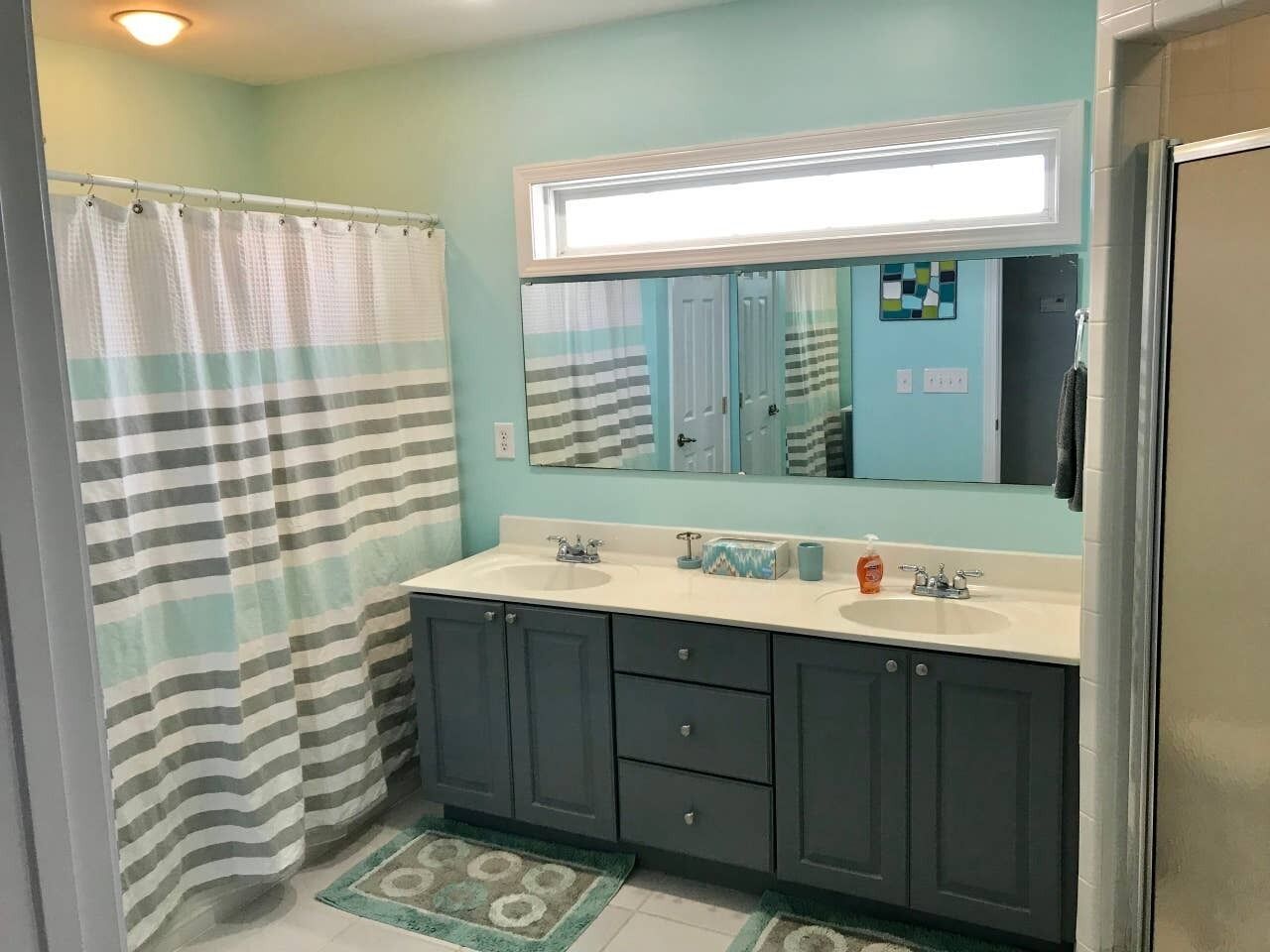 Une salle de bain avec un rideau de douche, deux lavabos, un miroir et un sol carrelé.