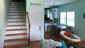 A staircase leading to a door labeled "BEACH HOUSE," a dining area with a table and chairs, and a kitchen with a window.