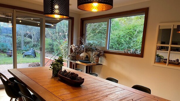 A spacious dining area with a wooden table, black chairs, and a large window offering a view of the garden.