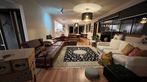 A modern living room with a brown leather sofa, a white sofa, and a black ottoman. There is a patterned rug on the floor.