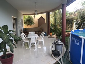 Eine überdachte Terrasse mit Tisch und Stühlen, ein Schwimmbad und ein Staubsauger.