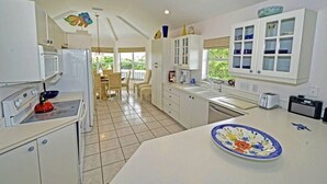Une cuisine avec des meubles blancs, un four à micro-ondes, une cuisinière et un évier. On y trouve également un coin repas avec des chaises et une table.