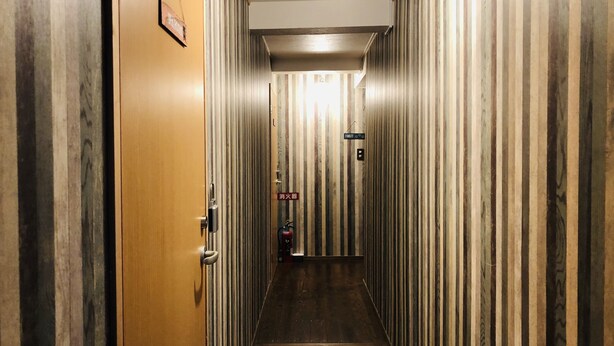 Um corredor estreito com paredes listradas e uma porta de madeira à esquerda.