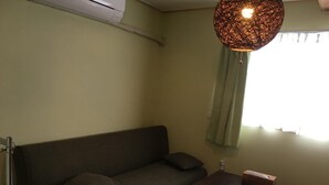Um quarto pequeno e com pouca luz, com um sofá, uma mesa de madeira e um lustre.
