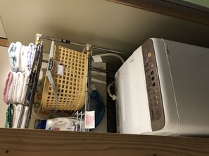 A washing machine with a control panel, a yellow laundry basket, and various towels hanging on a rack.