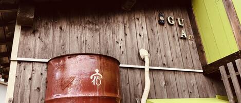 A rustic wooden building with a large red barrel labeled "Ama" and a green structure to the right.