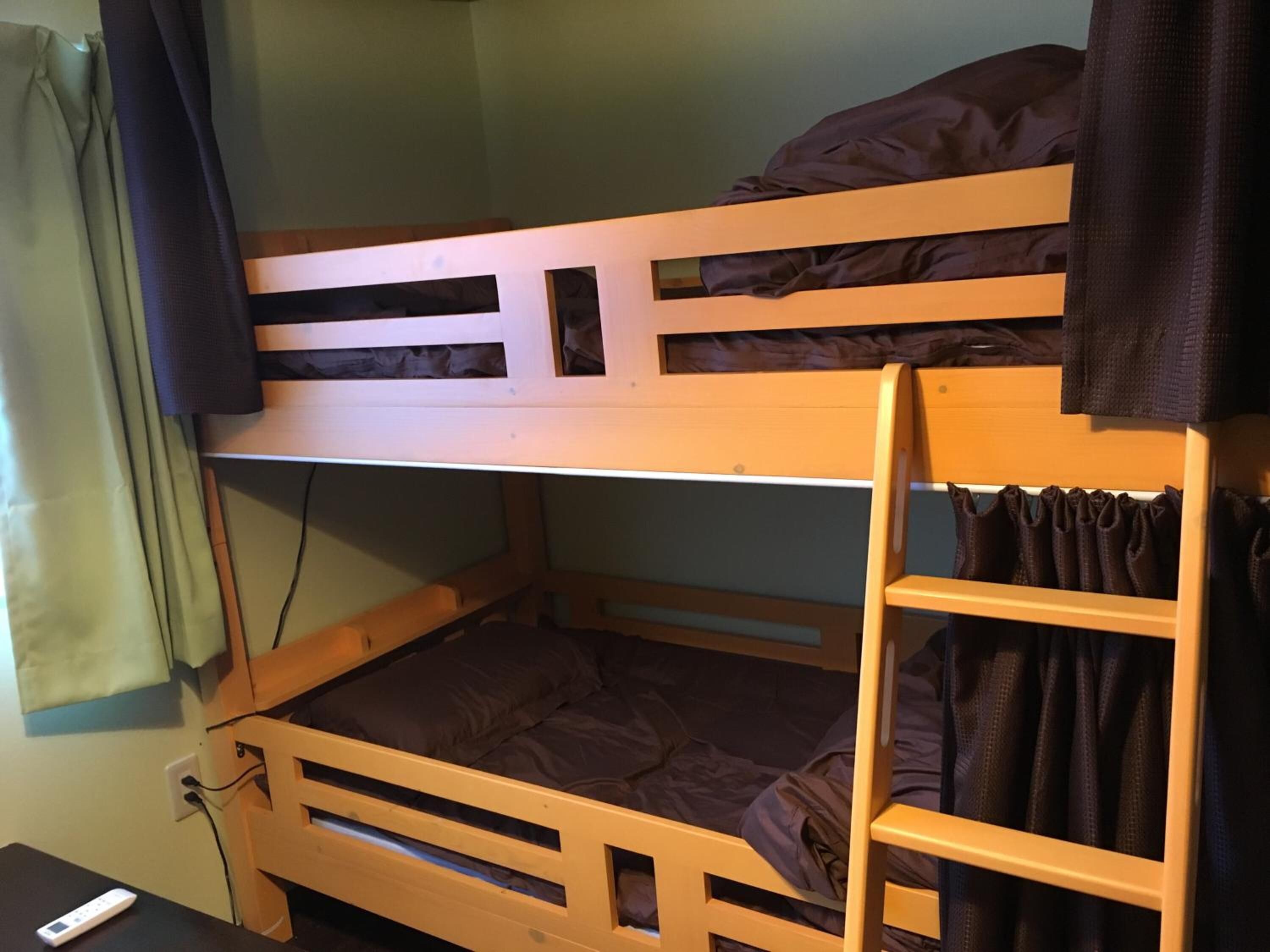 A bunk bed with a ladder, a desk with a remote control, and a curtain.