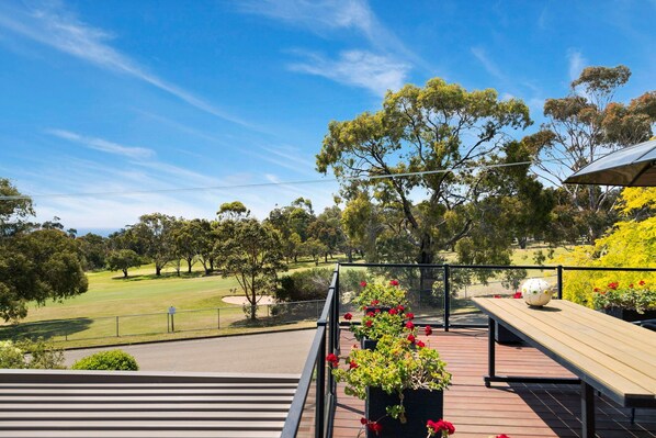 Une terrasse avec vue sur un terrain de golf, un grand arbre et une table de pique-nique.