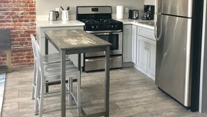 Une cuisine moderne avec des meubles gris, un réfrigérateur en acier inoxydable, un four à micro-ondes, une cuisinière et une table à manger avec des chaises.