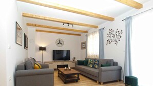 Una sala de estar moderna con dos sofás, una mesa de centro, un televisor y vigas de madera en el techo.