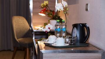 A hotel room with a wooden desk, a chair, a tray with cups, bottles, and a kettle.