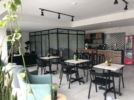 Un comedor moderno con sillas negras y mesas blancas, una zona de cocina con un salpicadero geométrico y un refrigerador rojo Coca-Cola.