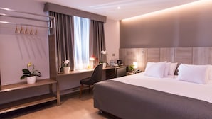 A hotel room with a large bed, a desk with a chair, a nightstand, and a potted plant. - Surya Lima (Lima)