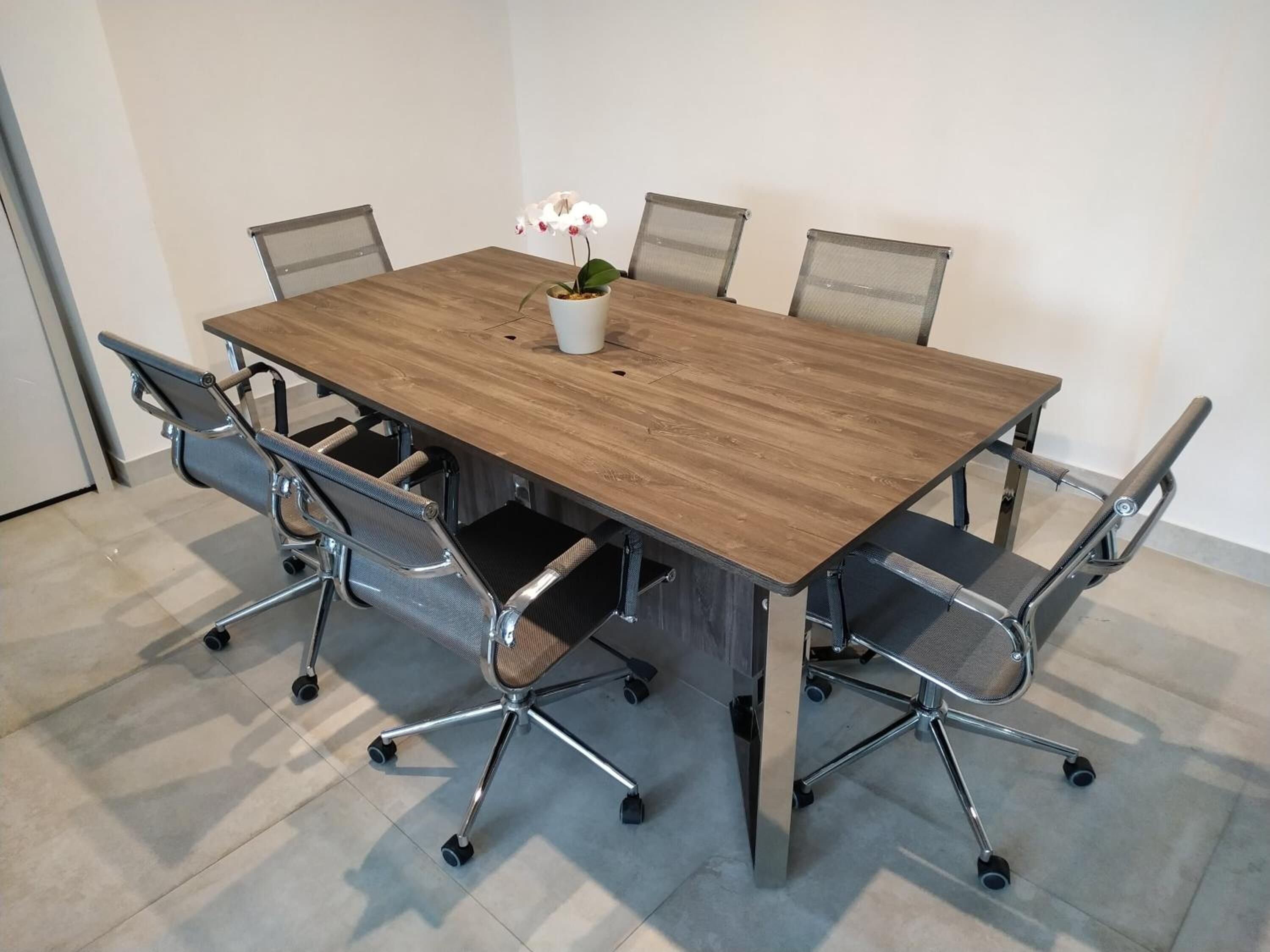 A conference table with a wooden top, surrounded by six mesh-backed office chairs with wheels.