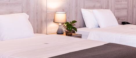A hotel room with two beds, a bedside lamp, a plant, and a phone on the nightstand.