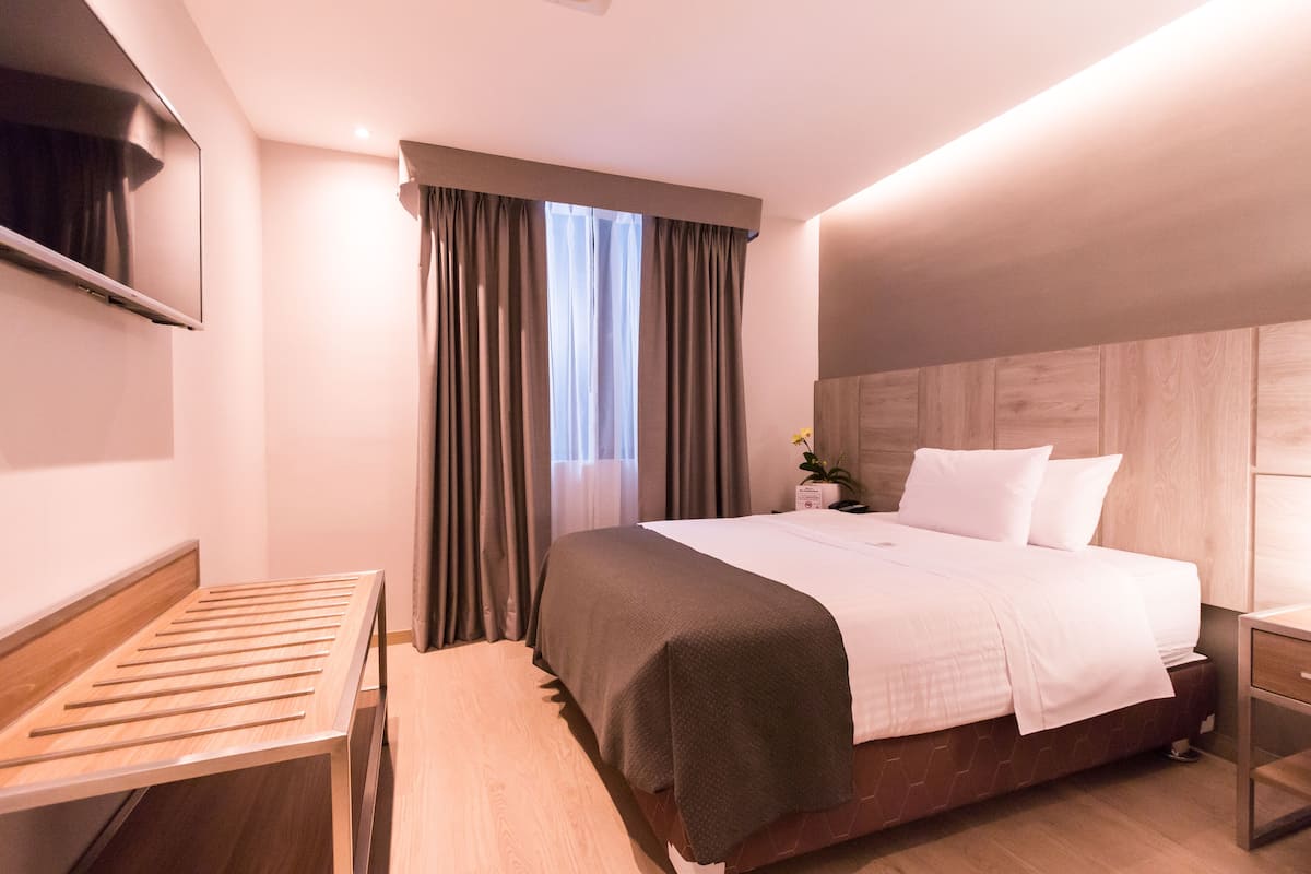 A modern hotel room with a bed, bedside table, and a TV mounted on the wall.