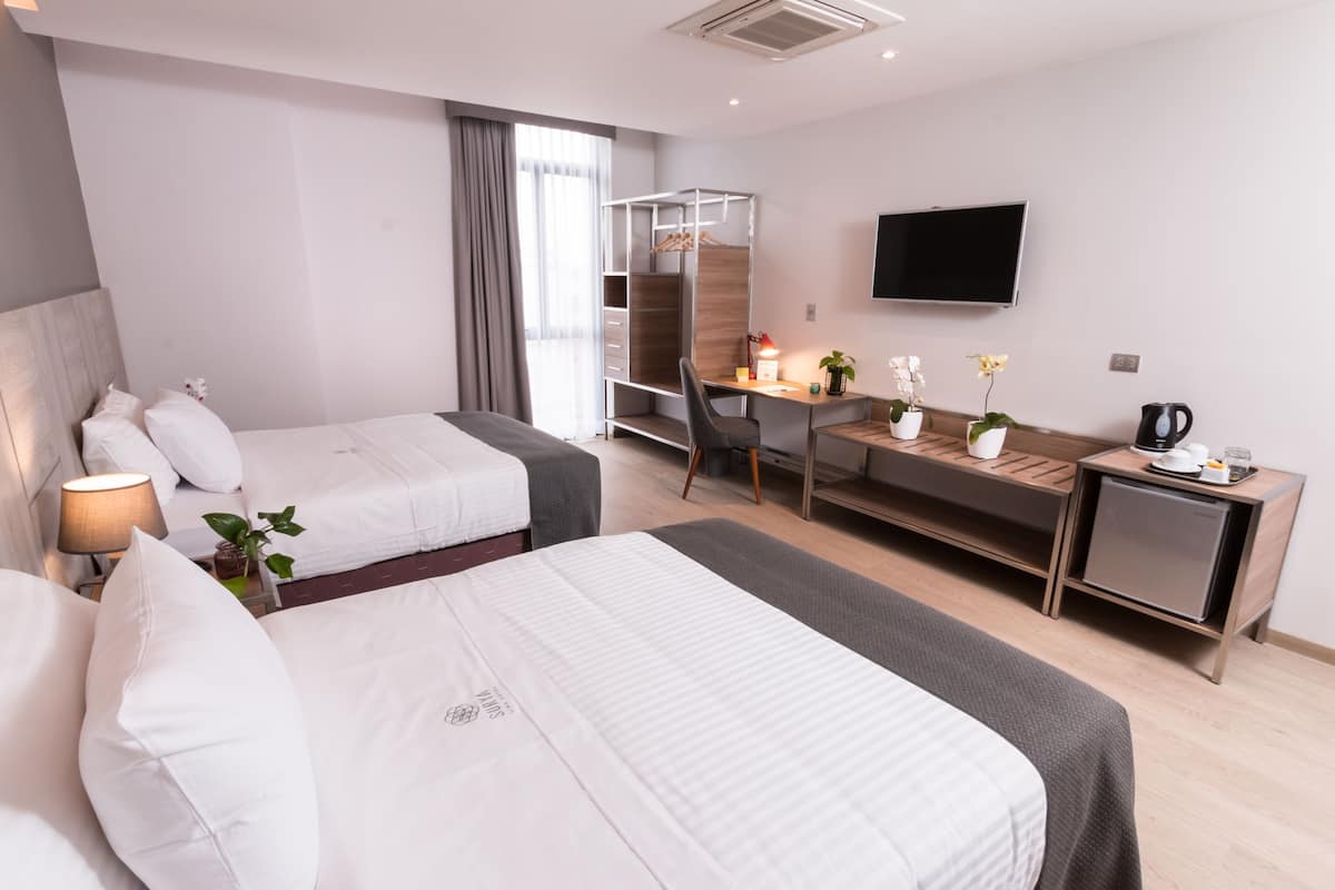 A hotel room with two beds, a desk, a TV, and a wardrobe.