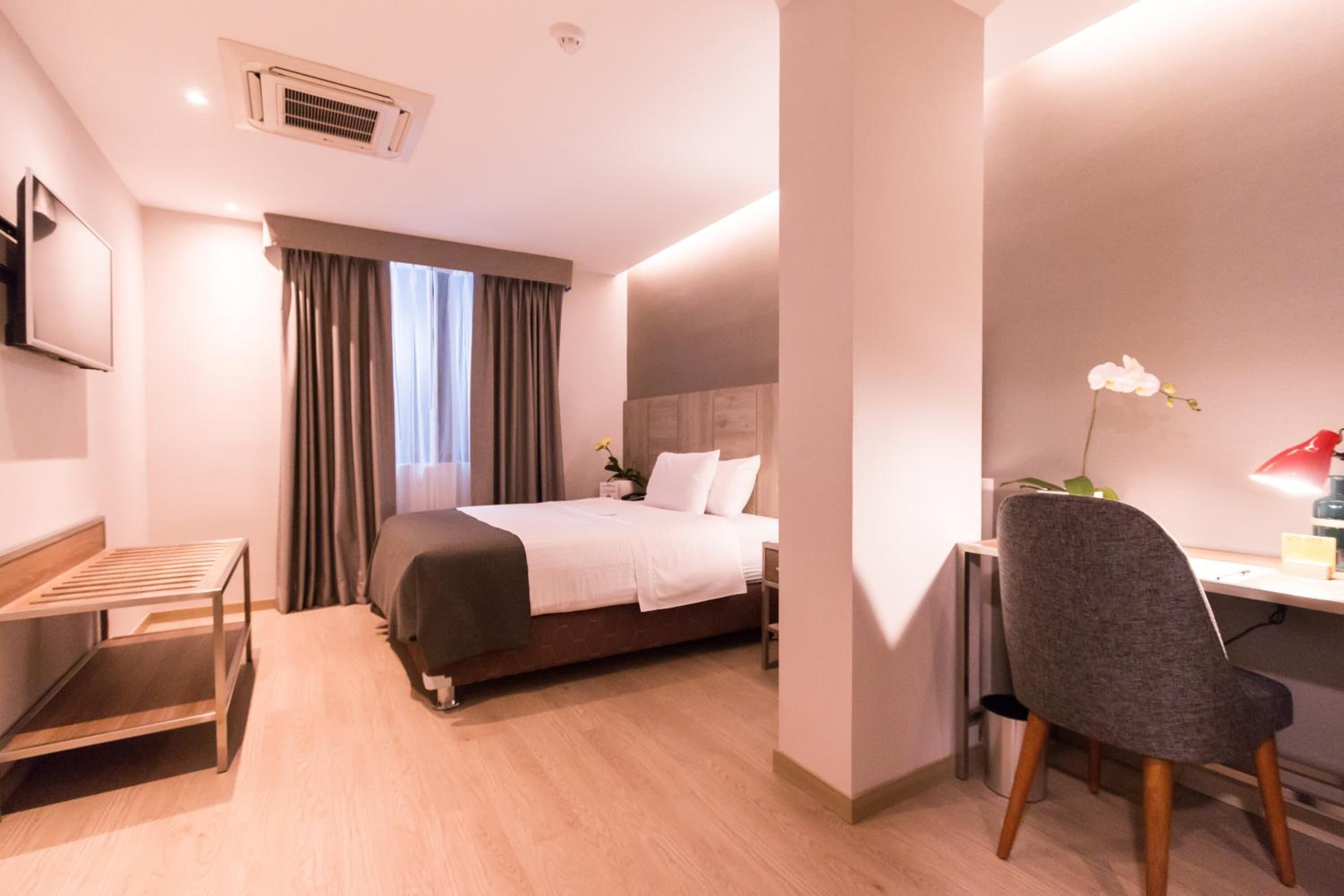 A hotel room with a bed, a desk, a chair, a TV, and a window with curtains.