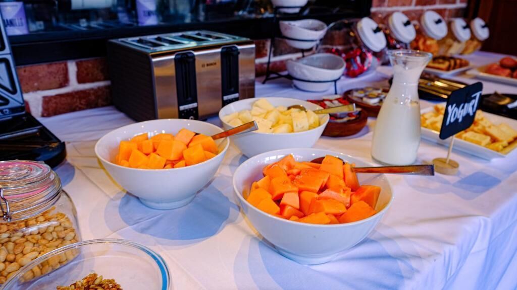 A buffet table with bowls of fruit, a milk jug, and a sign indicating a yogurt station.