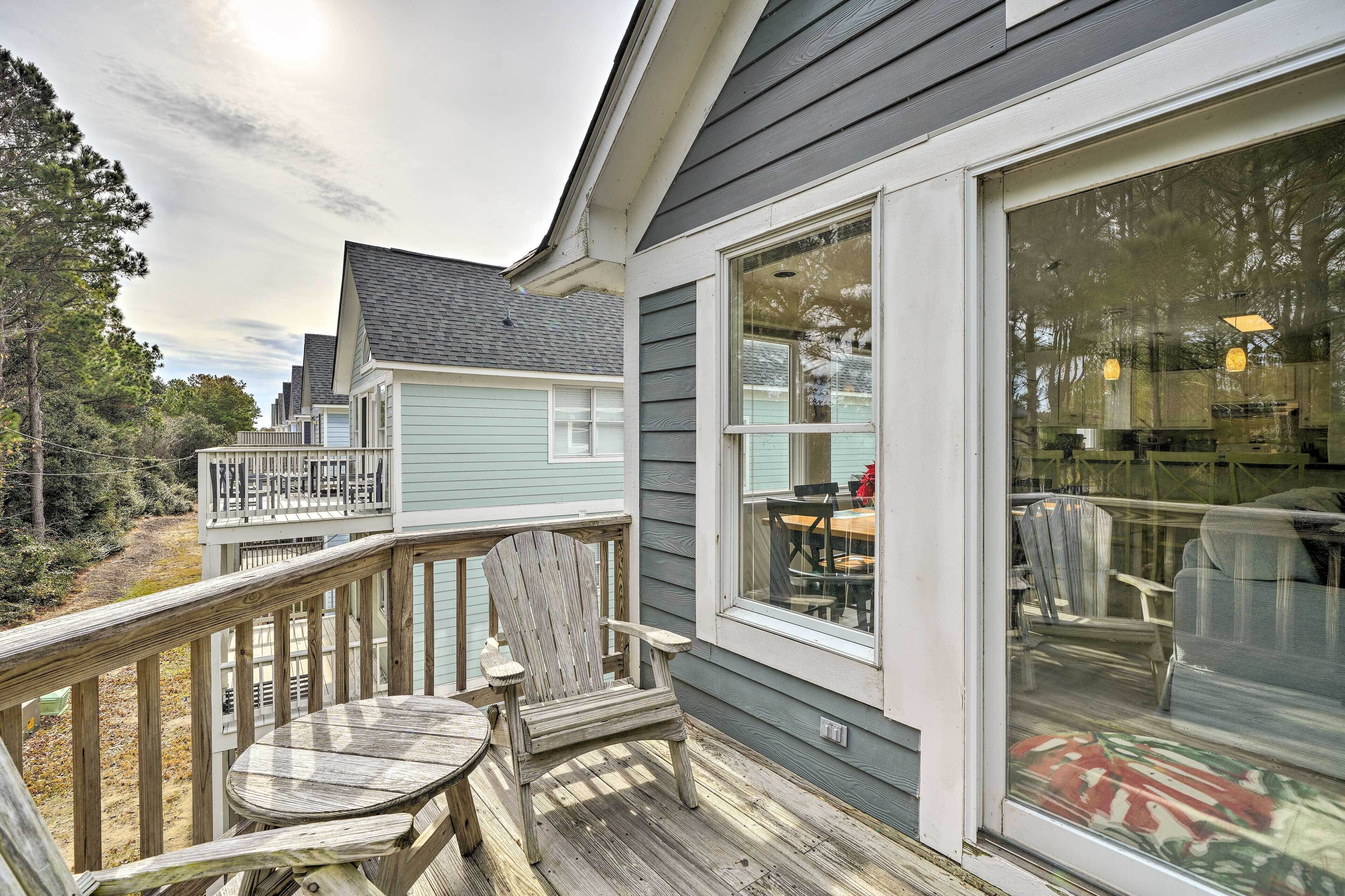 A wooden deck with a table and chairs, a glass door leading inside, and a view of the surrounding area.
