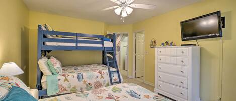 A bedroom with bunk beds, a ceiling fan, a television, and a dresser.
