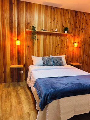 A wooden-paneled room with a bed, two wall-mounted lamps, and a shelf with a plant.