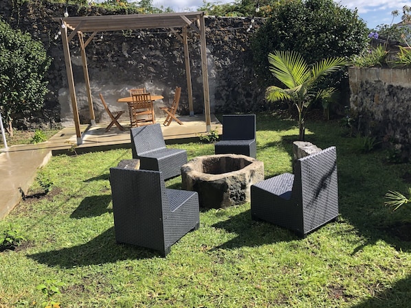 Relax in a shaded pergola with wicker chairs and a stone fire pit, perfect for casual dining or socializing.