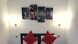 A neatly made bed with red and white bedding, two red pillows, and a set of towels on the bed. There are two bedside tables, one on each side of the bed. Above the bed, there are three framed pictures on the wall. - Luks Apartments (London)