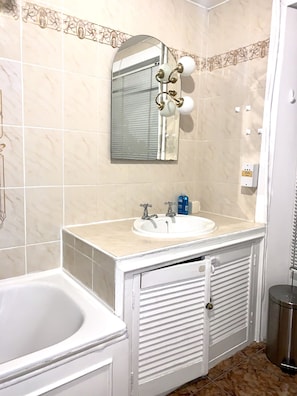 A bathroom with a white sink, mirror, and vanity. There is a bathtub and a shower area. - Luks Apartments (London)