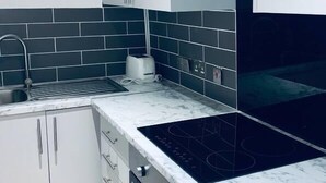 A modern kitchen with white cabinets, a black tiled backsplash, a built-in oven, and a black induction cooktop. - Luks Apartments (London)