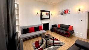 A living room with a grey sofa, a black and red sofa, a coffee table, and a fireplace. - Luks Apartments (London)