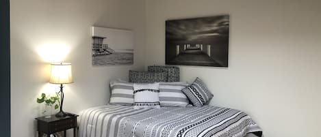 Une chambre à coucher comprenant un lit, une table de chevet avec une lampe et deux œuvres d’art accrochées au mur.