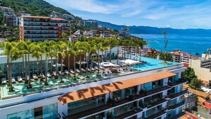 Un hotel con piscina en la azotea, varios balcones y vistas al mar.