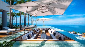 Zona junto a la piscina con sillones de descanso y sombrillas, con vista a un océano azul y transparente.