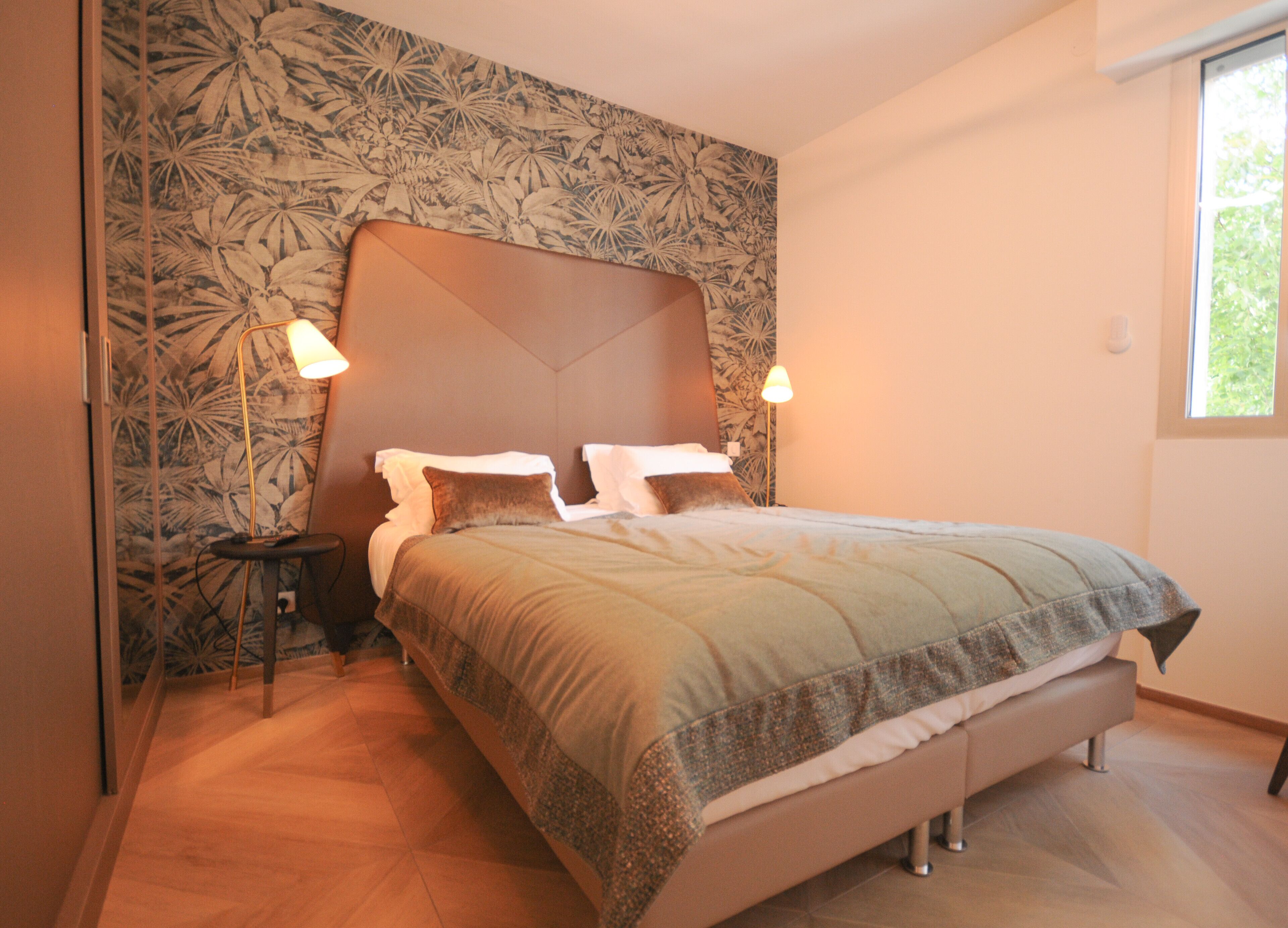 Un dormitorio con una cama grande, dos lámparas de noche, un papel tapiz floral y una ventana.
