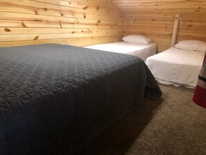 A small, cozy room with two single beds, a wooden ceiling, and a carpeted floor.