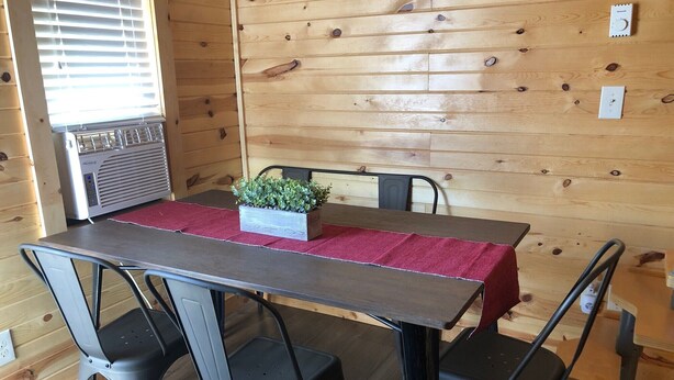 A wooden interior with a table, chairs, a radiator, and a window with blinds. - Frenchy's Hideaways Cabin #6 (Custer)