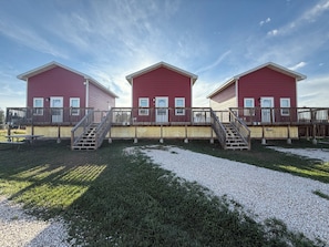 A row of red buildings with a wooden deck and stairs leading to a covered area. - Frenchy's Hideaways Cabin #6 (Custer)