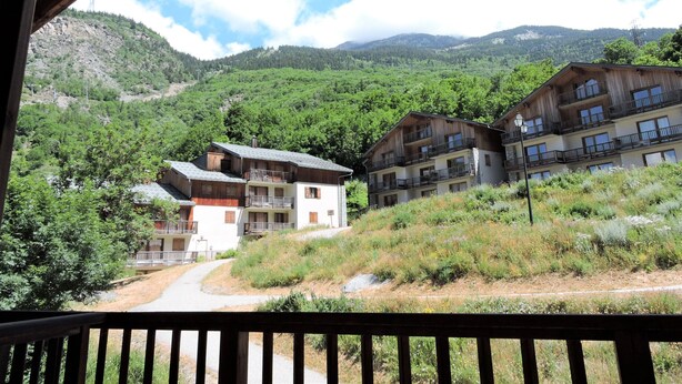 Un complejo turístico de montaña con edificios de madera, balcones y una vista despejada de las colinas circundantes.