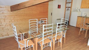 Un comedor con una mesa de vidrio y sillas blancas, paredes de madera y una cocina con pileta y alacenas.