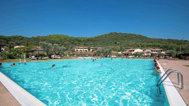 Une grande piscine à l’eau d’un bleu limpide, entourée de bâtiments et de verdure.